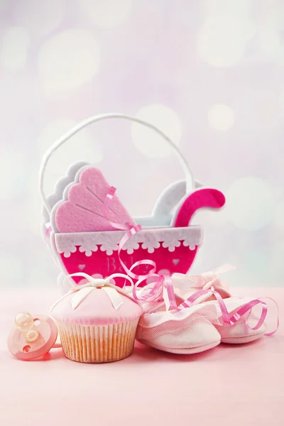 Tasty cupcakes with bow and baby shoes, decorative baby carriage on color background — Stock Photo, Image