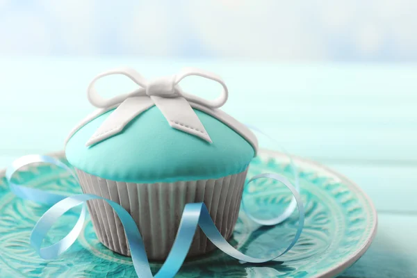 Leckerer Cupcake mit Schleife auf farbigem Holztisch, auf hellem Hintergrund — Stockfoto