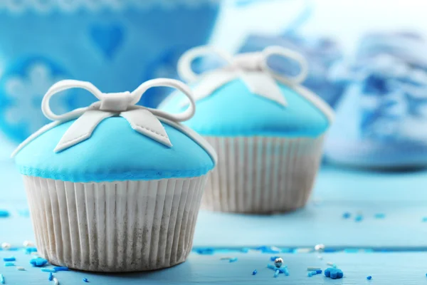 Välsmakande cupcake med båge och baby skor på färg trä bakgrund — Stockfoto