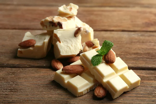Части белого шоколада с орехами на фоне цвета дерева — стоковое фото