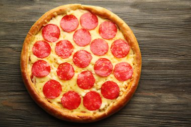 Ahşap arka planda salamlı lezzetli bir pizza.