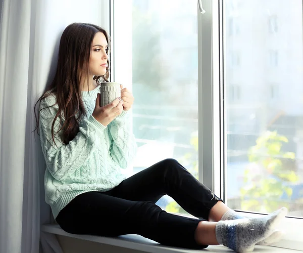 Hübsche Frau sitzt mit Tasse Kaffee auf dem Fensterbrett — Stockfoto