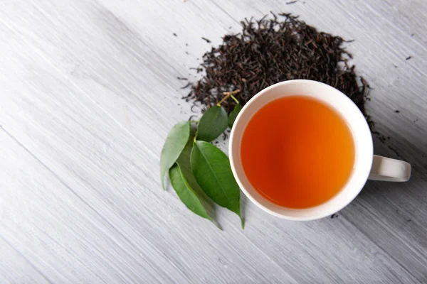 Taza de té de cerámica con hojas de té dispersas sobre fondo de madera claro — Foto de Stock