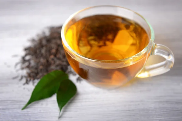 Üveg csésze fekete tea, zöld levelek a szürke fából készült háttér — Stock Fotó