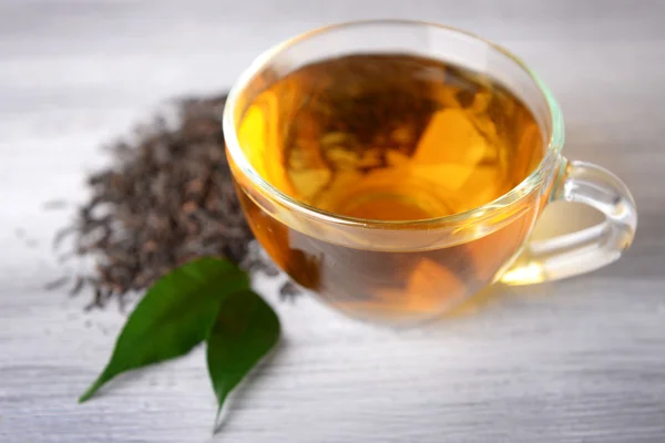 Glass cup of black tea with green leaves on grey wooden background — Stock Photo, Image