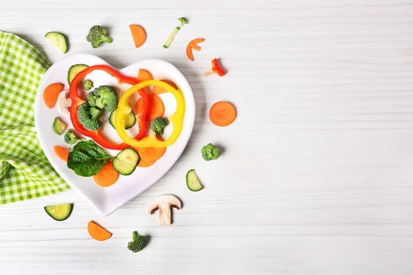 Faydalı ahşap masa üstten görünüm üzerinde kalp şeklinde bir tabakta sebze kesme — Stok fotoğraf