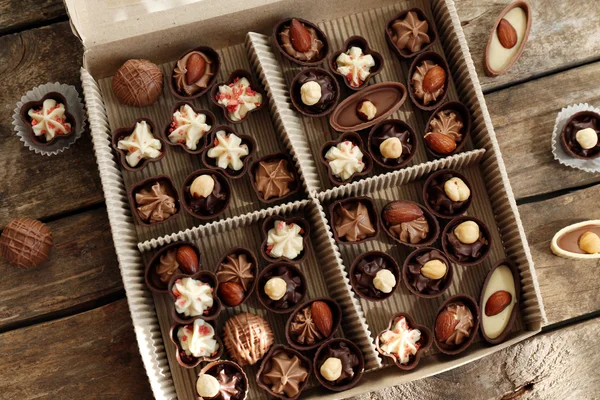 Different chocolate candies in paper box on wooden background, close up — Stock Photo, Image