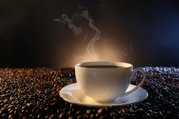 Taza de café caliente entre granos de café sobre fondo oscuro — Foto de Stock