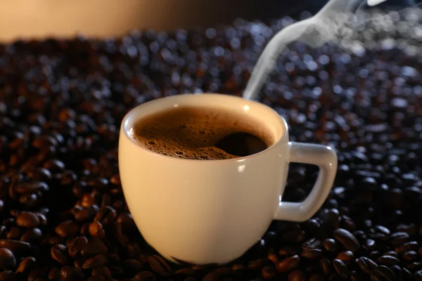 Tasse heißen Kaffee zwischen Kaffeebohnen auf dunklem Hintergrund — Stockfoto