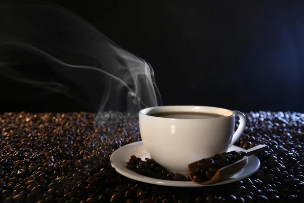 Cup of hot coffee among coffee beans on dark background Stock Image