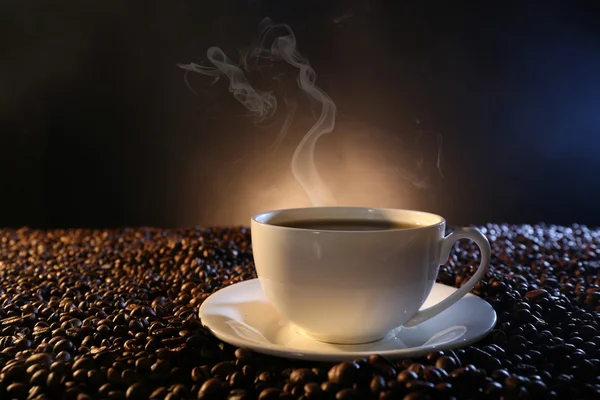 Cup of hot coffee among coffee beans on dark background Stock Picture