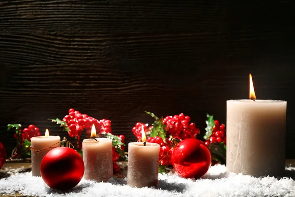 Velas ardientes y accesorios navideños con nieve sobre fondo de madera —  Fotos de Stock