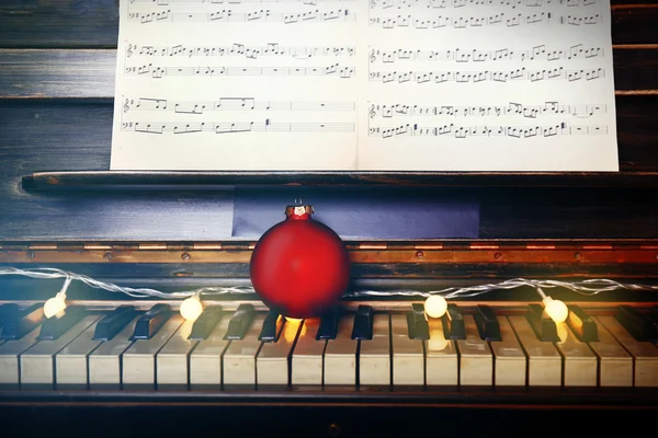 Tasti di pianoforte decorati con luci di decorazione e palla rossa, primo piano — Foto Stock