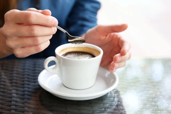 Tazza di caffè con le mani e cucchiaio sul tavolo in sfondo caffè — Foto Stock