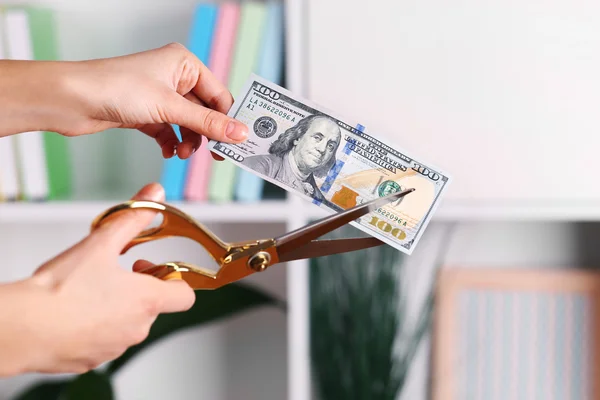 Mani con forbici taglio banconota da un dollaro, su sfondo interno sfocato — Foto Stock