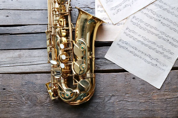 Saxofone dourado bonito com notas musicais em fundo de madeira, close-up — Fotografia de Stock