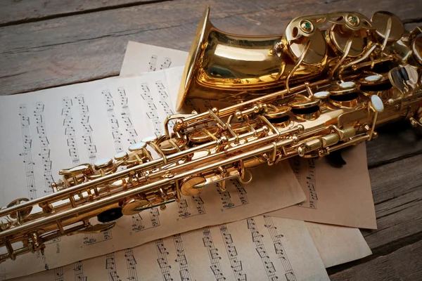 Beautiful golden saxophone with musical notes on wooden background, close up — Stock Photo, Image