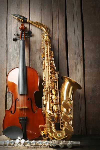 Musical instruments: saxophone, violin and flute with notes on wooden background — Stock Photo, Image