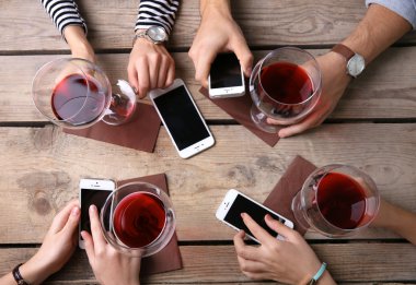 Kırmızı şarap, gözlüklü ahşap masa arka planda tutarak akıllı telefonlar ile dört el