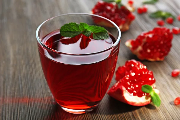 Um copo de suco saboroso e fruta granada, em fundo de madeira — Fotografia de Stock