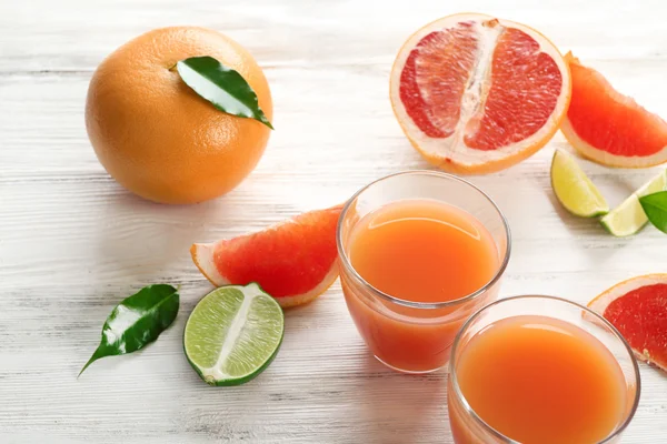 Two glasses of citrus juice and fresh fruits on light wooden background — Stock Photo, Image