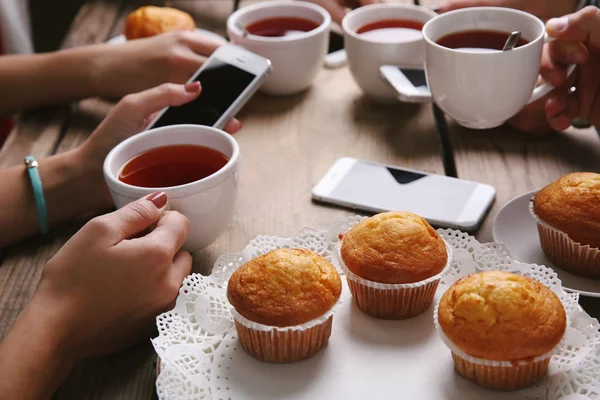 Okos telefonok csésze tea, fából készült asztal háttér gazdaság négy kézre — Stock Fotó