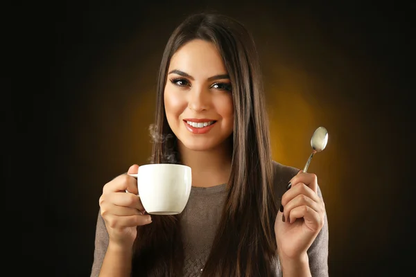 Joyeux belle femme avec tasse de café et cuillère sur fond sombre — Photo