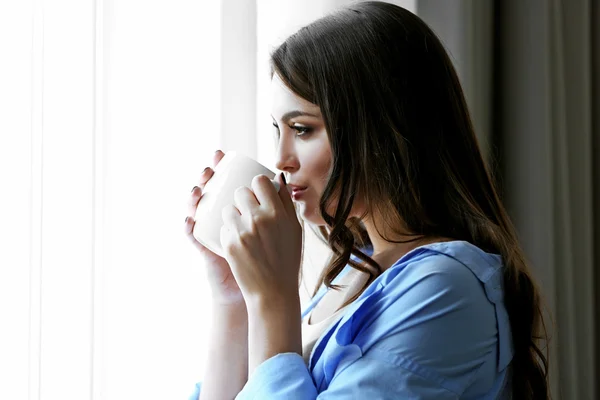 Femme avec tasse de café debout près de la fenêtre dans la chambre — Photo