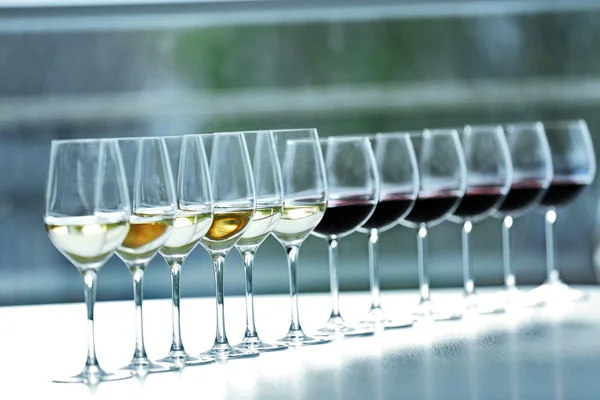 Wijnglazen met witte en rode wijn op houten tafel op lichte achtergrond — Stockfoto