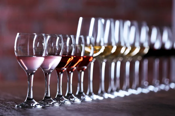 Wijnglazen met wit, rood en roze wijn op houten tafel op muur steen achtergrond — Stockfoto