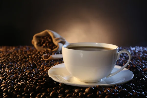 Xícara de café quente entre grãos de café — Fotografia de Stock