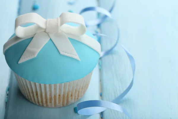 Tasty cupcake with bow on color wooden background — Stock Photo, Image