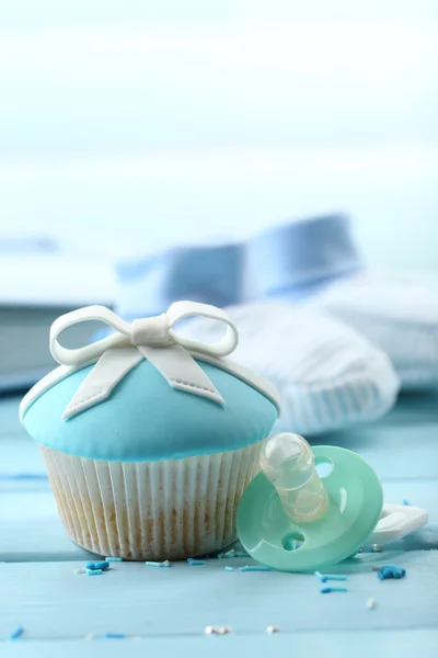 Tasty cupcake with bow and baby shoes on color wooden background — Stock Photo, Image