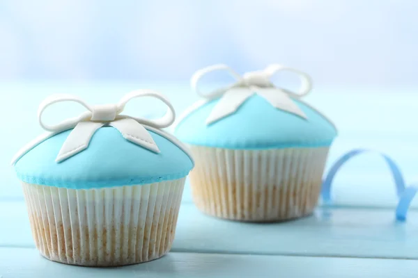 Sabroso cupcake con lazo en la mesa de madera de color, sobre fondo brillante — Foto de Stock