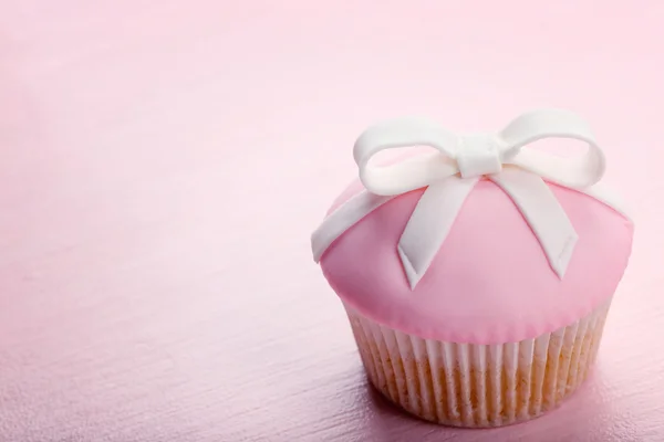 Tasty cupcake with bow on color wooden background — Stock Photo, Image