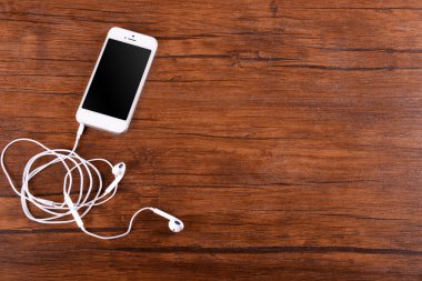 Kulaklıklarla vernikli ahşap arka plan üzerinde beyaz cep telefonu