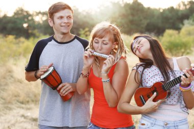 Müzik aletleri ormandaki açık havada oynarken mutlu gülümseyen arkadaşlar