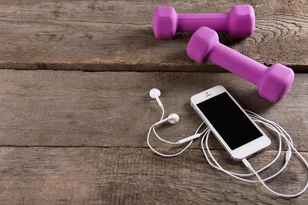 Vit mobiltelefon med hörlurar och rosa dum klockor på trä bakgrund — Stockfoto