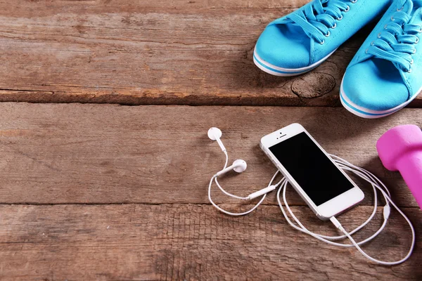 Celular branco com fones de ouvido e sinos burros rosa e gumshoes no fundo de madeira — Fotografia de Stock