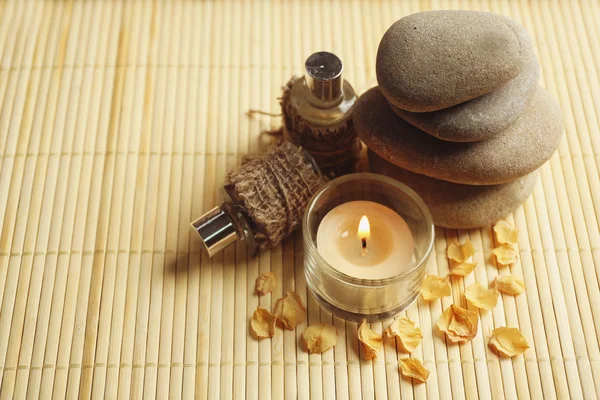 Beautiful composition with candle, aroma oil and pebbles on bamboo mat — Stock Photo, Image