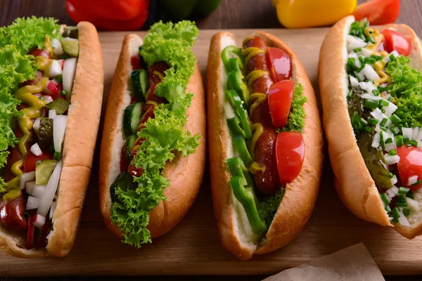 Hot dogs and vegetables on wooden cutting board — Stock Photo, Image