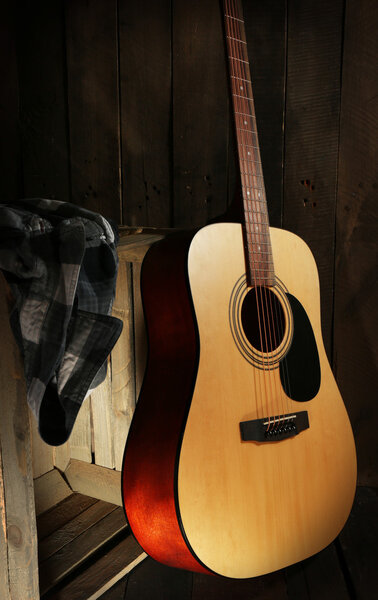 Guitar and shirt left on crate on wooden wall background