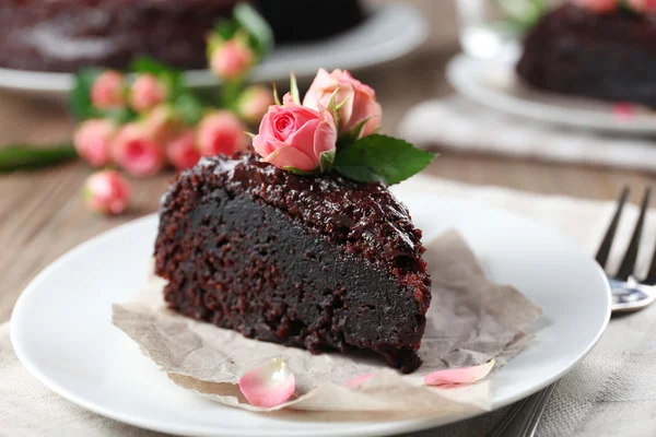 Stuk chocolade cake versierd met bloemen op bruin houten tafel — Stockfoto