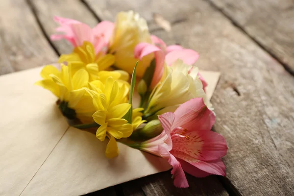 Fresh bouquet of flowers in envelope on wooden background — Stock Photo, Image