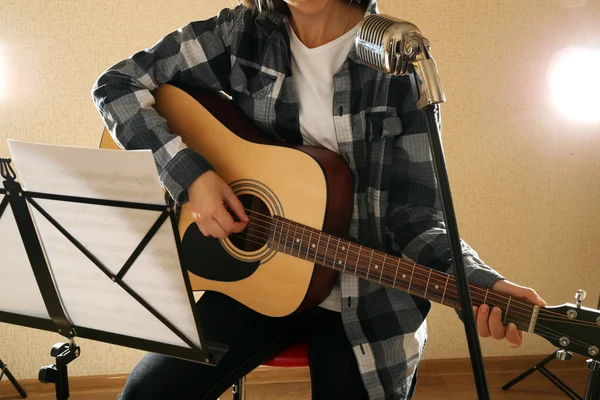 Músico toca la guitarra en estudio de luz con soporte de notas musicales, de cerca — Foto de Stock