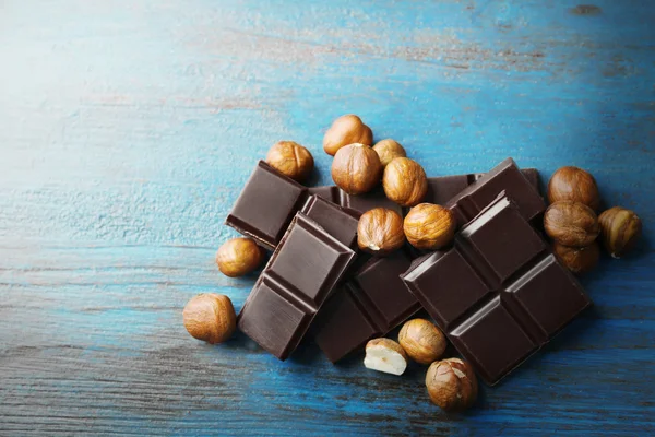 Pedaços de chocolate preto com nozes na cor de fundo de madeira — Fotografia de Stock