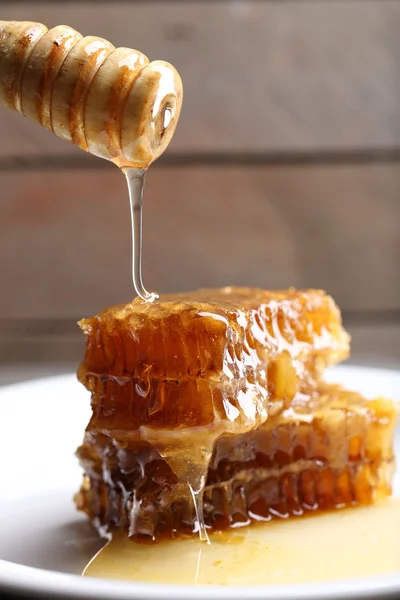 Miele gocciolante su favi su piatto su fondo di legno — Foto Stock