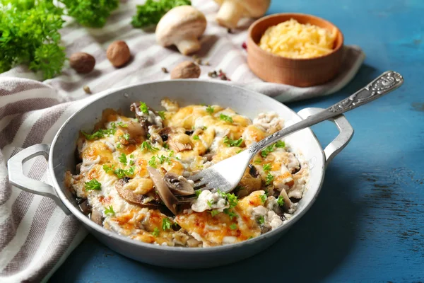 Cogumelos assados, frango e queijo gratinado na panela, na cor de fundo de madeira — Fotografia de Stock
