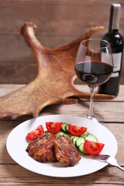 Roasted venison fillet and fresh vegetables on plate, on wooden background