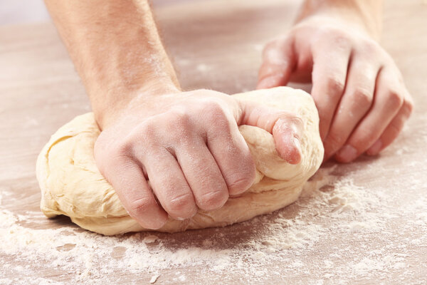 Hands kneading dough for pizza on the wooden table, close-up